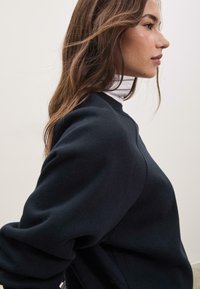 Felpa navy con scollo rotondo e maniche lunghe, caratterizzata da una texture liscia e da dettagli di cucitura discreti sulle spalle.