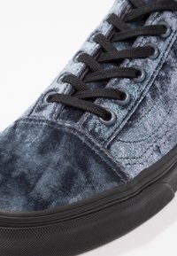 Gros plan d'une basket en velours bleu avec des lacets noirs et une semelle en caoutchouc noire texturée.