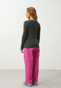 Getailleerde donkergroene trui met lange mouwen, gecombineerd met losse roze broek. De broek heeft een gestructureerde afwerking en wordt gedragen met grijze sneakers.