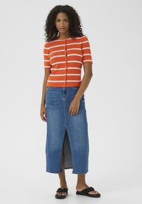 Cardigan à manches courtes rayé orange et blanc avec des boutons, associé à une jupe maxi en denim bleu avec une fente à l'avant. Sandales noires à enfiler.