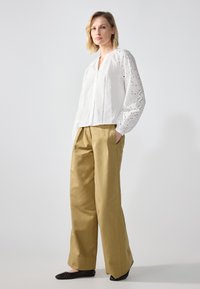 White blouse with embroidered detailing and puff sleeves, paired with loose khaki trousers. Black flat shoes complete the outfit.