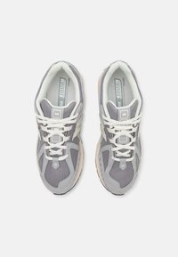 Ljusgrå träningsskor i mesh och syntetmaterial. Reflekterande detaljer, vadderad mellansula och vita snören. Modell NB 1906.