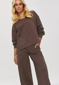 Brązowy sweter z luźnym krojem i długimi rękawami, zestawiony z dopasowanymi spodniami o szerokim nogawce. Gładka faktura, prosty design, bez widocznych wzorów.