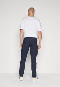 Pantaloni de cargo Navy cu mai multe buzunare laterale, realizați dintr-un material durabil. Asociați cu un tricou alb cu mânecă scurtă și încălțăminte casual.