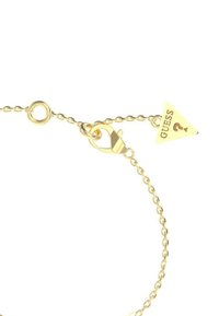 Goudkleurige kettingarmband met een kreeftsluiting en een driehoekig label met "GUESS" en een vraagtekenicoon.