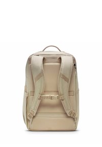 Beige rygsæk med polstrede skulderremme, et håndtag øverst og justerbare spænder. Glat stof med et tekstureret design og sidelommer.