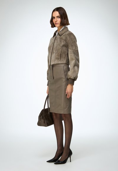Smeđa privučena jakna od brušene kože s patentnim zatvaračem, uparena s uskom olivno zelenom kožnom olovka suknjom. Crne štikle i teksturirana smeđa torba.