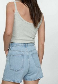 Světle modré džínové šortky s vysokým pasem, pětikapsový design, rozdrbaný lem a jemné vyblednutí. Doplněné šedým žebrovaným tílkem.