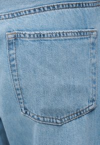 Κοντινό πλάνο ανοιχτόχρωμου τζιν παντελονιού που δείχνει τσέπη στην πλάτη με λεπτομερή ραφή και υφή υφάσματος.