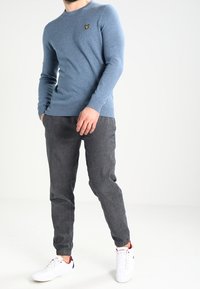 Maglione azzurro chiaro lavorato a maglia con collo rotondo; pantaloni grigi con fantasia; sneakers bianche con accenti rossi e navy. Piccolo logo sul maglione.