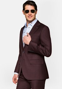 Bordowy w kratę garnitur z klapami typu notch, w połączeniu z jasnoniebieską koszulą w kolorowe wzory ptaków. Model w okularach przeciwsłonecznych.