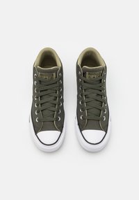 Zelené plátěné tenisky s bílým gumovým špičkou a podešví, s kovovými očky a klasickým šněrovacím designem. Viditelné logo Converse All Star.