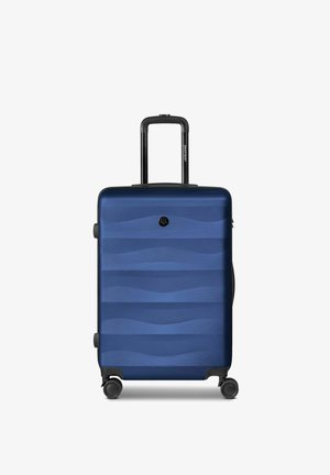 Maleta rígida azul marino con patrón de ondas, asa telescópica y cuatro ruedas giratorias, de pie sobre un fondo blanco.