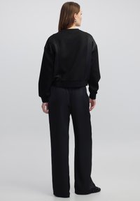 Schwarzes Sweatshirt mit lockerer Passform und Rundhalsausschnitt, kombiniert mit weiten schwarzen Hosen. Beide Kleidungsstücke haben eine glatte Textur und ein minimales Design.