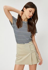 T-shirt a righe navy e bianche abbinato a una mini gonna beige con due decorativi dettagli a fibbia e un design plissettato.