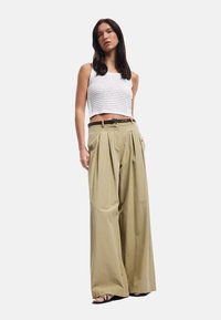 Hæklet cropped top i hvid, parret med højtaljede, plisserede brede bukser i lys beige. Udsmykket med et brunt bælte.