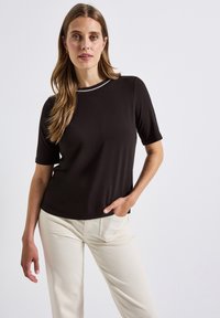 Black short-sleeve top with a rounded neckline featuring a contrasting light-colored trim, paired with off-white pants. Smooth, stretchy fabric.