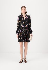 Abito nero a fiori con scollatura a V, maniche lunghe a palloncino e vita arricciata. Abbinato a sandali neri con cinturini e una piccola borsa beige.