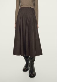 Gonna A-line marrone con vita alta, realizzata in tessuto testurizzato, con dettagli delle cuciture. Abbinata a stivali neri in pelle al ginocchio.
