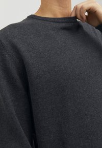 Dunkelgrauer Pullover mit Rundhalsausschnitt, strukturierter Strickware und überschnittenen Schultern, der ein einfaches und minimalistisches Design präsentiert.