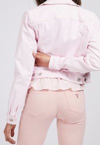 Chaqueta de mezclilla rosa claro con dobladillo con volantes, cierre de botones y mangas largas, combinada con pantalones ajustados rosa claro que tienen bolsillos traseros.