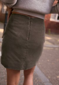 Olive green corduroy skirt with a fitted design, rear zipper closure, and subtle ribbed texture. Hemline falls above mid-thigh.