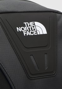 Gros plan d'un sac à dos noir avec un tissu texturé et un logo The North Face blanc sur un panneau noir moulé.
