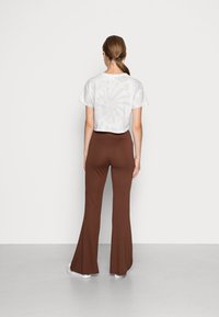 T-shirt blanc court avec un motif gris clair tourbillonnant ; pantalon évasé marron ajusté ; modèle de dos, mettant en valeur la silhouette de l'ensemble.