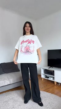 Camiseta blanca de gran tamaño con un estampado gráfico colorido de un sol y olas. Pantalones de pierna ancha negros. Color sólido, textura de tela suave.