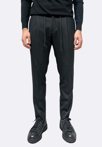 Pantaloni neri a taglio dritto, design plissettato, vita con coulisse e texture sottile. Abbinati a scarpe nere con suola spessa.