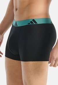 Černé boxerky s tyrkysovým pasem, na kterém je logo a texturovaný vzor, vyrobené z elastické látky pro pohodlí.