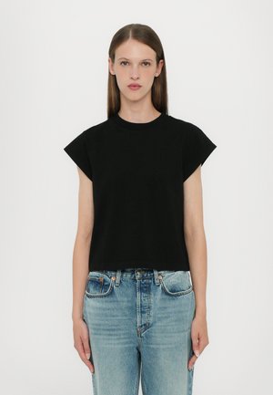 Black cropped t-shirt with short, rolled sleeves. Made of soft cotton, featuring a round neckline and a relaxed fit. Paired with light blue jeans.