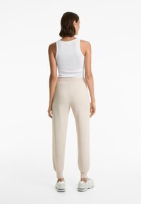 White ribbed tank top paired with beige knit joggers featuring elastic waistband and tapered cuffs, worn with white sneakers.