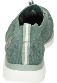 Chaussure slip-on tricotée verte avec une surface texturée, semelle en caoutchouc blanche et une languette à l'arrière avec deux rayures blanches.