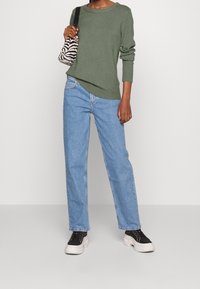 Grön stickad tröja med rund halsringning, ljusblå raka jeans och svarta sneakers med vita sulor. En zebra-mönstrad väska avslutar outfiten.