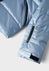 Svijetloplava jakna s kvadratnim uzorkom, rukav s crnim patentnim zatvaračem i podesivom čičak trakom na manžeti, na bijeloj pozadini.