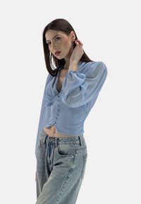 Hellblaue, kurze Bluse mit Puffärmeln, vorderen Knöpfen und tiefem Ausschnitt, kombiniert mit hochtaillierten, ausgewaschenen Jeans.