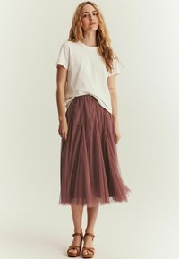 Vit kortärmad t-shirt i kombination med en flödande, knälång mauve tullekjol och bruna klacksandaler. En enkel, avslappnad outfit.