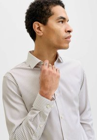 Chemise à rayures boutonnée en beige clair avec des rayures étroites foncées. Caractérisée par un col classique, des manches longues et des poignets à boutons. Texture lisse.