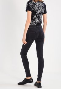 Jeans negros ajustados con cintura alta, combinados con una camiseta negra que presenta un patrón de rosas blancas en la parte trasera. Unos zapatos de cuero negros completan el look.