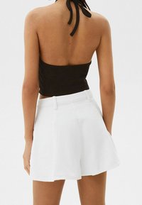 Svart ribbad halterneck-top med ryggsnörning, i kombination med vita högmidjade shorts med en slät yta och flared design.