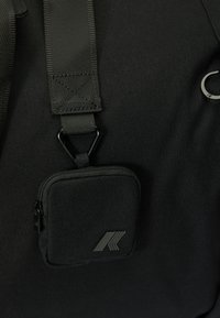 Black fabric bag featuring a detachable small pouch with a zipper and logo, adjustable straps, and a metal clip attachment.