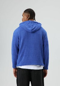 Blauwe, gestructureerde hoodie gemaakt van fleece, voorzien van een capuchon, lange mouwen en een losse pasvorm, gecombineerd met een donkere spijkerbroek.