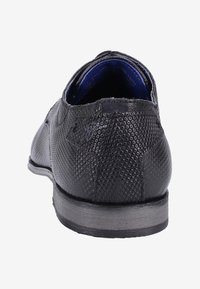 Chaussure habillée en cuir noir texturé vue de l'arrière, montrant un motif hexagonal en relief et une semelle foncée avec une doublure intérieure bleue.