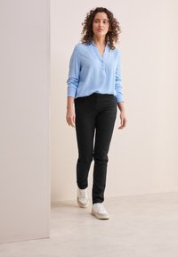 Blusa azul claro con un escote de botones, combinada con jeans negros ajustados y zapatillas blancas. Tejido suave y corte relajado.