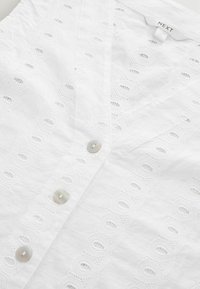 Robe en coton blanc avec des motifs découpés brodés, une fermeture à boutons et une encolure en V. Texture lisse avec des détails subtils.