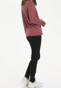 Rosa langärmliges Shirt mit Rundhalsausschnitt, kombiniert mit schwarzen Slim-Fit-Jeans und weißen sportlichen Sneakers. Einfaches Design, minimale Details.
