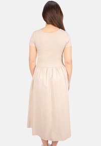 Beiges Kleid mit einem gerippten Körper, kurzen Ärmeln und einem fließenden, gerafften Rock, der unterhalb des Knies endet. Glatte Textur, minimale Hardware.