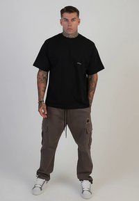 Zwart T-shirt met korte mouwen en een ronde hals. Gecombineerd met losvallende, kaki cargobroeken met twee zijzakken. Witte sneakers.