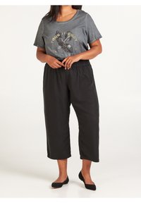 Mörkgrå t-shirt med tryck av örn, tillsammans med lösa svarta cropped byxor. Slät textur och elastisk midja. Svarta lägenheter på fötterna.